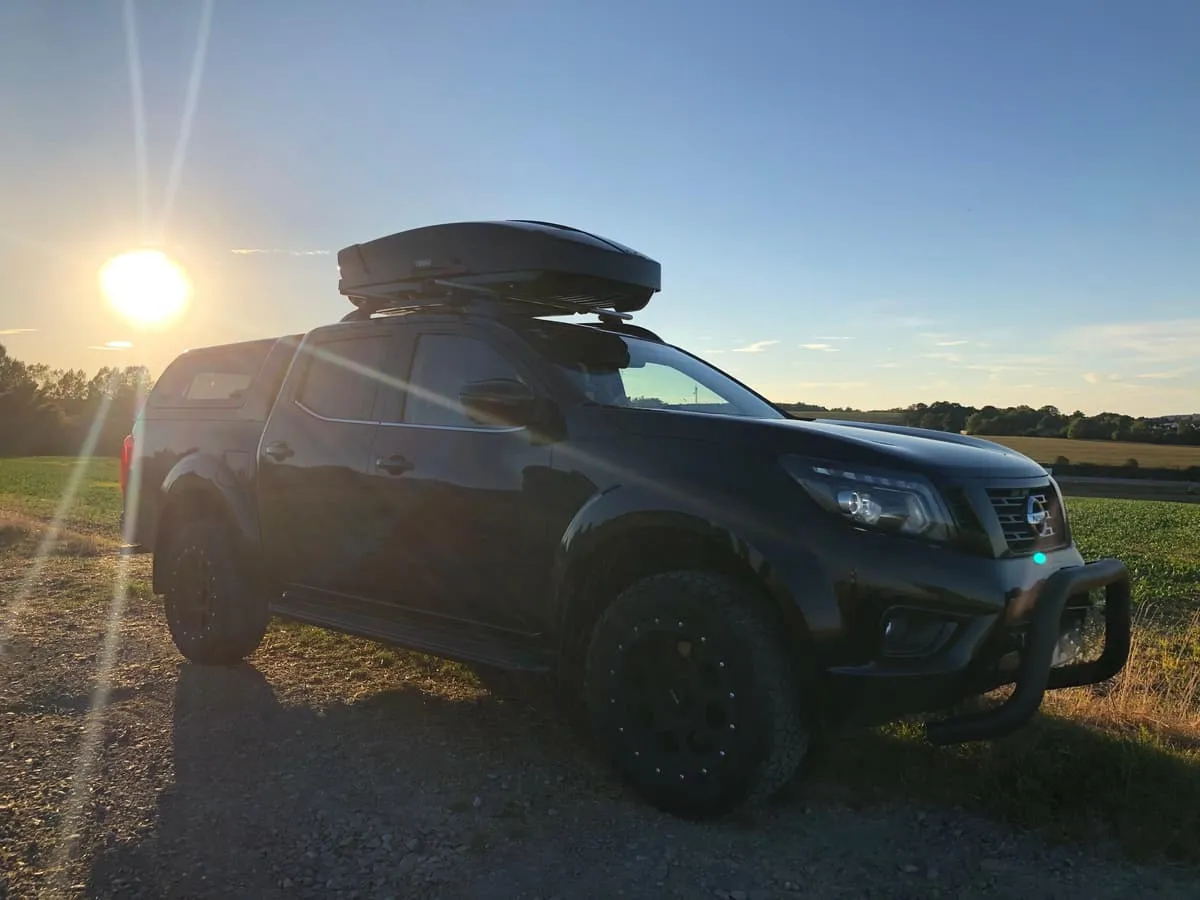 Schwarzer Pickup mit montierter Thule-Dachbox im Gegenlicht der Abendsonne auf einem Feldweg