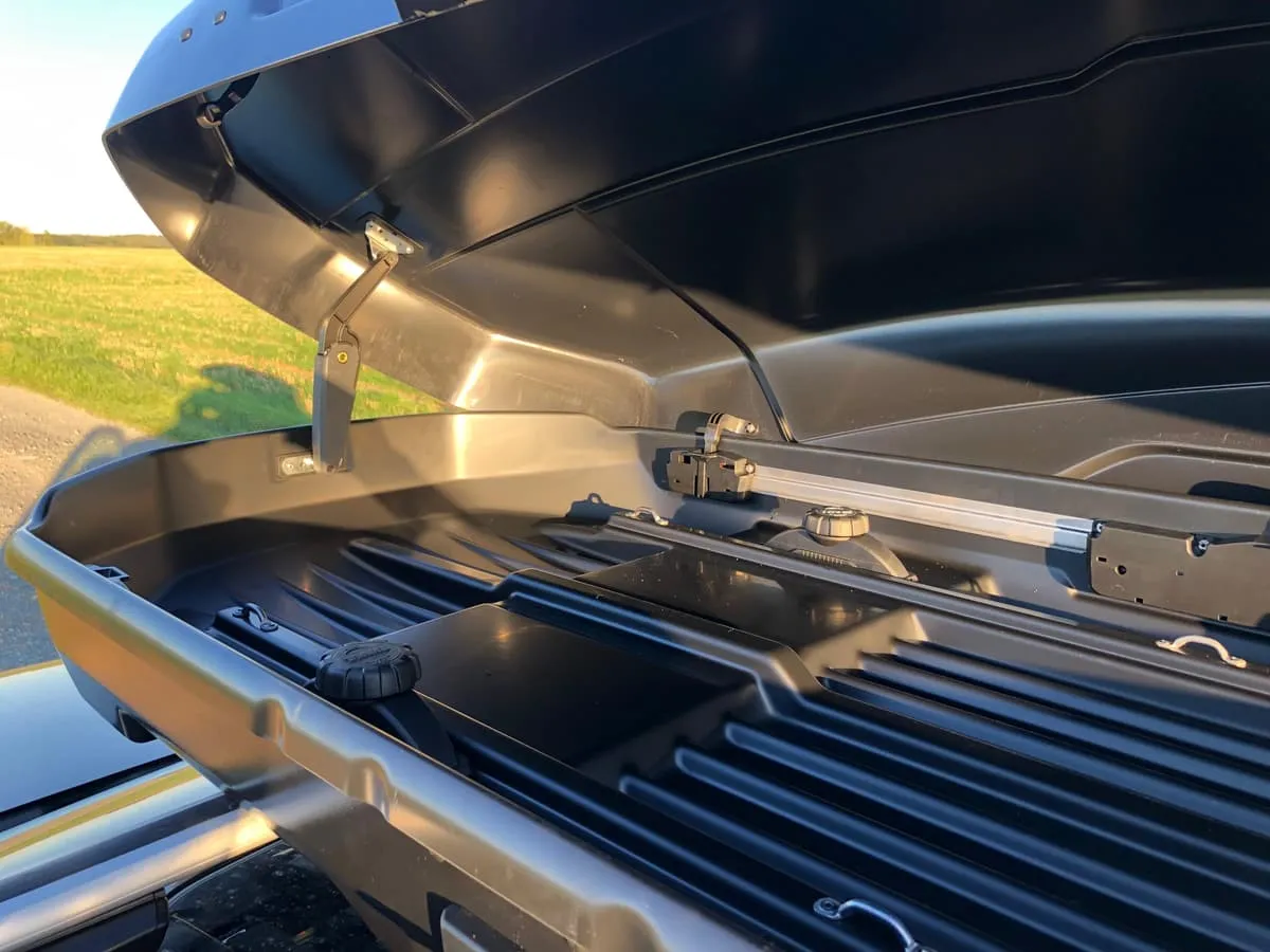 Geöffnete Dachbox auf dem Autodach: Deckelstütze, Befestigungsschiene und Schnellspanner im Innenraum