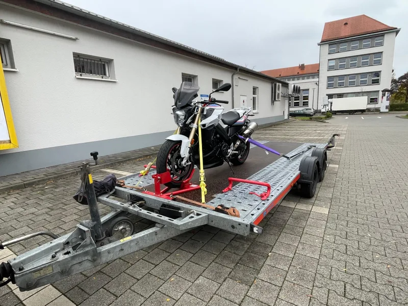 Motorrad, aufrecht verzurrt auf dem Anhänger vor einer Halle